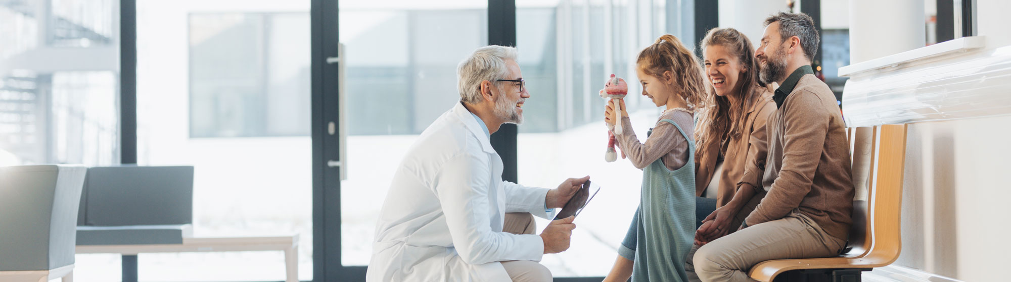 Doctor kneeling and talking to small girl with family sitting behind her.